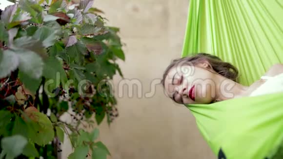 快乐的年轻女子轻松地躺在阳台上的吊床上女人在吊床上晒太阳视频的预览图