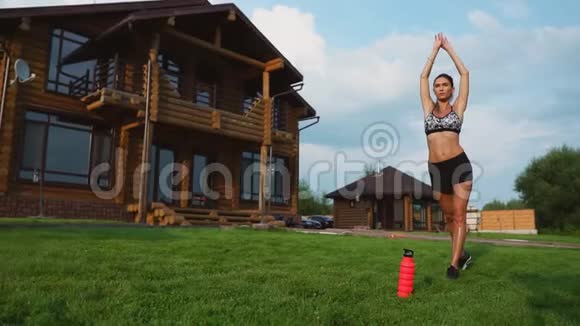 女人在草地上做瑜伽背景是一座美丽的房子健康生活方式的概念视频的预览图