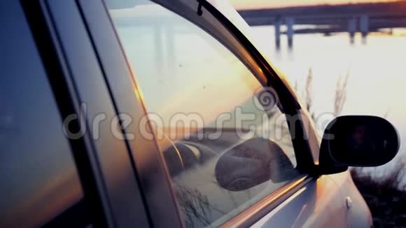 那人在车里打开一扇窗户欣赏着桥上河边美丽的日落坐在停车场里视频的预览图