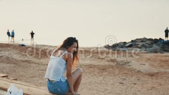 快乐的年轻女子坐在清晨的沙滩上欢笑视频的预览图