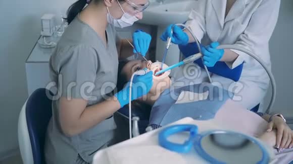 坐在牙科椅上的年轻女人医生与牙科护士治疗病人缩放和抛光牙齿视频的预览图