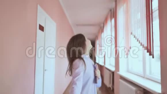 快乐的女孩带着一本书沿着学校走廊跑视频的预览图