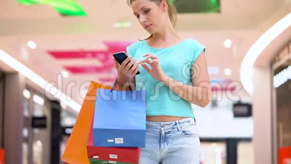 在购物中心用智能手机装纸袋的女人视频的预览图