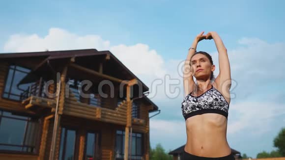 女人在草地上做瑜伽背景是一座美丽的房子健康生活方式的概念视频的预览图