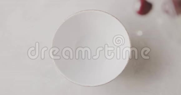 成熟的红色樱桃与水滴从一个白色的桌子上的玻璃容器掉进一个白色的陶瓷碗顶级视频的预览图