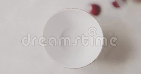 成熟的红色樱桃与水滴从一个白色的桌子上的玻璃容器掉进一个白色的陶瓷碗顶级视频的预览图