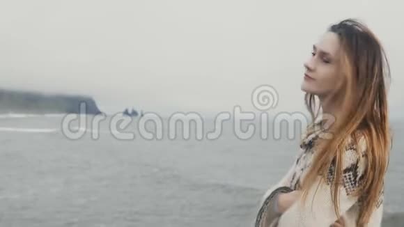 年轻漂亮的女人站在黑色的海滩上微笑着享受冰岛巨魔脚趾岩石的景色视频的预览图