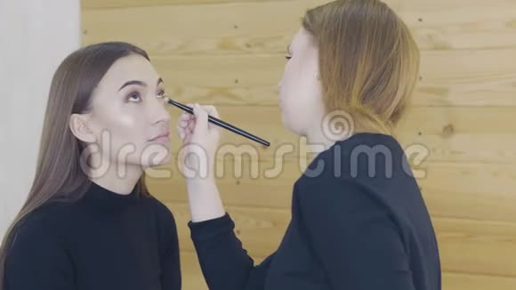 专业化妆师在白色房间内将眼线涂在模特的整个眼睛上美容化妆和时尚视频的预览图