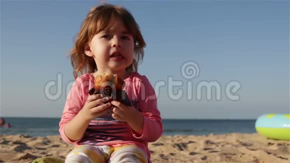 一个可爱的小孩子吃蛋糕喝瓶子里的水她坐在沙滩上靠海视频的预览图