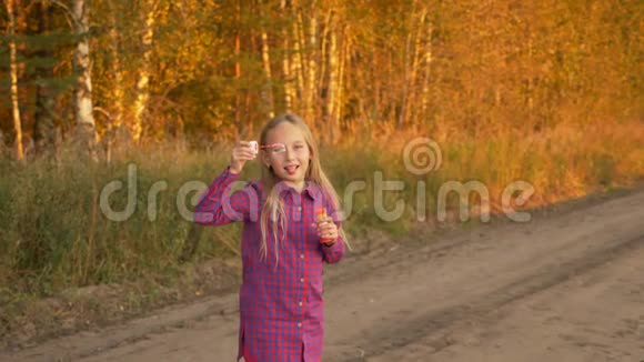 快乐的年轻女孩吹着肥皂泡扭动着转过身来户外秋天慢动作视频的预览图