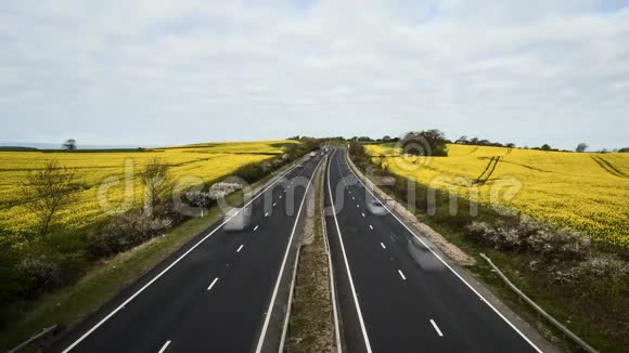 盛开的油菜花田之间的乡村高速公路交通繁忙视频的预览图