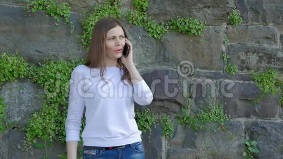 在智能手机上说话的漂亮女孩背景中野生石头的复古墙视频的预览图