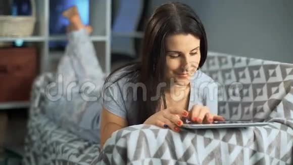 漂亮的女人在家里躺在沙发上用平板电脑视频的预览图
