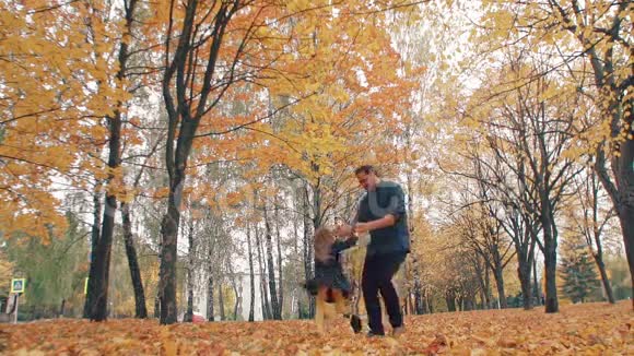 年轻英俊的父亲把他可爱的小女儿转过来牵着她的手秋天公园慢莫视频的预览图