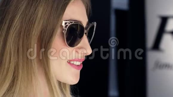 女孩高个子漂亮的金发女人在一家时尚的商店里试着戴太阳镜精品店在前面欣赏自己视频的预览图
