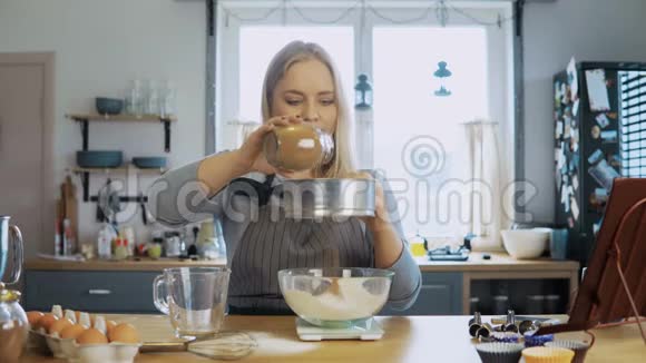 年轻漂亮的女人重可可加上面粉女孩用厨房的天平碗和筛子做这个视频的预览图
