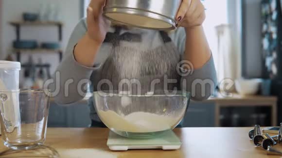 这位年轻美女的特写镜头用厨房的天平碗和筛子称面粉视频的预览图