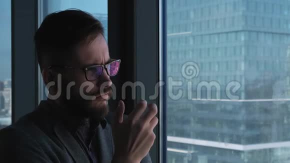 年轻的成功商人留着胡子在俯瞰市中心的窗户背景下思考高业务视频的预览图