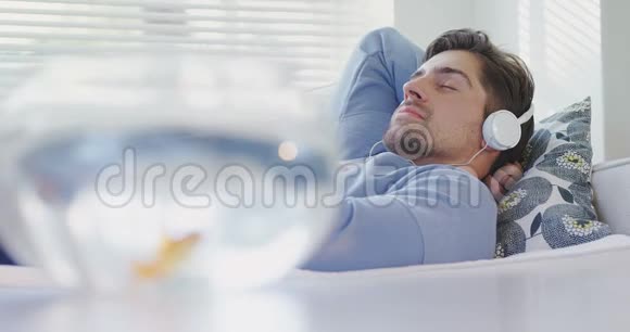 黄金鱼缸和男人躺在沙发上戴着耳机上面放着音乐4K4k视频的预览图