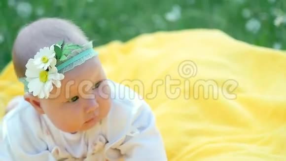 一个漂亮的小女孩宝贝躺在一个黄色的格子上躺在草地上她的头上有一条用洋甘菊做的绷带视频的预览图
