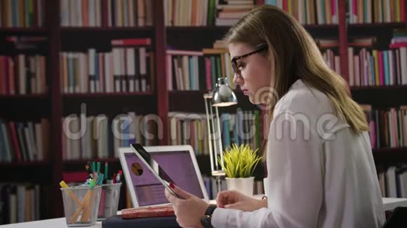 一位女士在图书馆里用笔记本电脑和平板电脑视频的预览图