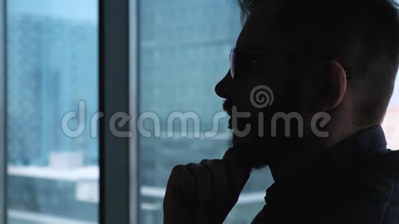 年轻的成功商人留着胡子在俯瞰市中心的窗户背景下思考高业务视频的预览图