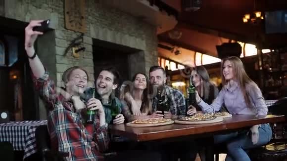 一群朋友在披萨店休息在披萨和啤酒的背景下自拍一个年轻人视频的预览图