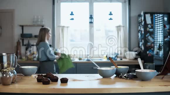 年轻的金发女人洗衣服烤完纸杯蛋糕后打扫厨房女性在家做甜点视频的预览图