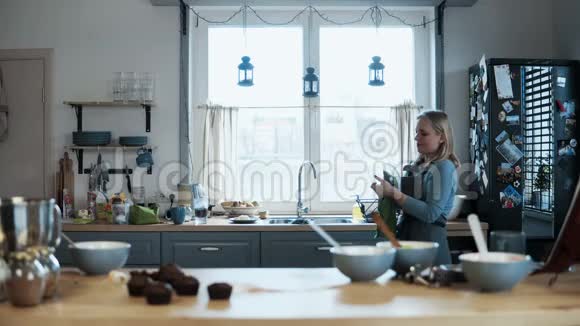 年轻漂亮的女人烤完纸杯蛋糕后洗碗金发女郎做饭后打扫厨房视频的预览图