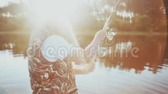 年轻人在湖边的橡皮船里钓鱼雄把一根鱼竿扔进水里把鱼卷拧开视频的预览图