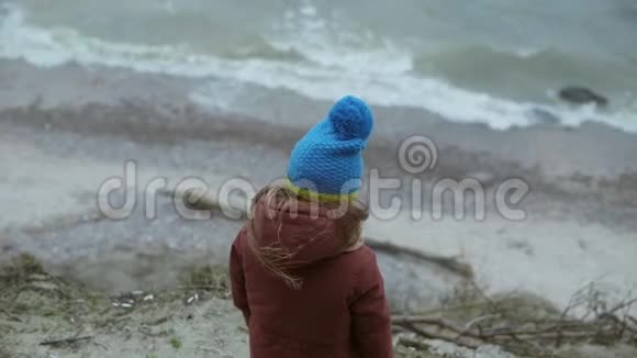 在寒冷的天气里站在海边的小女孩的后景独自一个孩子望着海浪做梦视频的预览图