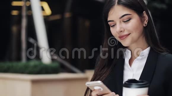 专业的年轻女商人站在城市街道上使用智能手机喝咖啡概念新业务视频的预览图