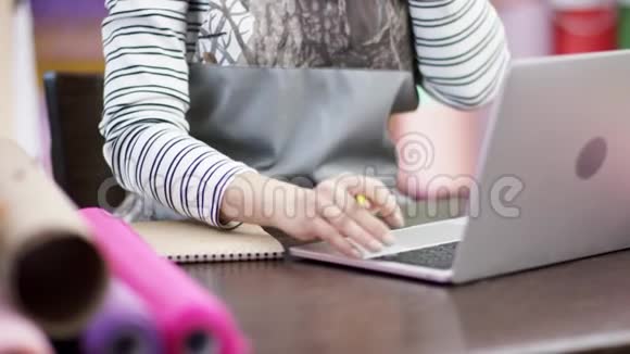 一个年轻的女人正在花店里工作她的笔记本电脑和电话快乐的花艺女人用纸包花视频的预览图