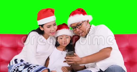 带圣诞帽的快乐家庭使用智能手机视频的预览图