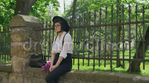 一个戴着帽子戴着眼镜的女孩坐在石栅栏上视频的预览图
