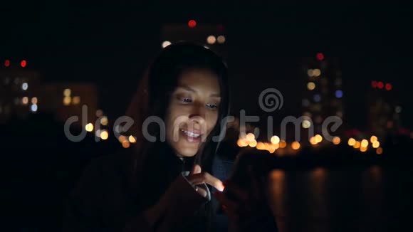 在夜城街道上使用手机的迷人的年轻混合种族微笑妇女慢动作4K莫斯科俄罗斯视频的预览图