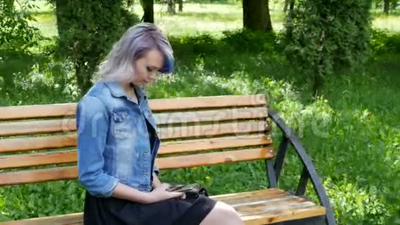 年轻的金发女孩有着专业的化妆和发型蓝色的头发穿着黑色的连衣裙穿着牛仔夹克坐着视频的预览图