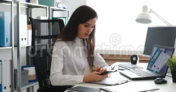 女商人用智能手机说话在现代办公室用笔记本电脑工作视频的预览图