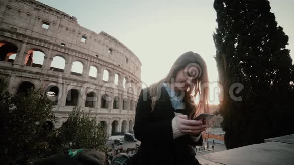 年轻迷人的女人站在意大利罗马的斗兽场附近使用智能手机微笑的女孩聊天视频的预览图