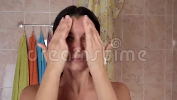 年轻女子涂防皱霜漂亮的女孩在浴室里把奶油涂在脸上有魅力的年轻女子视频的预览图