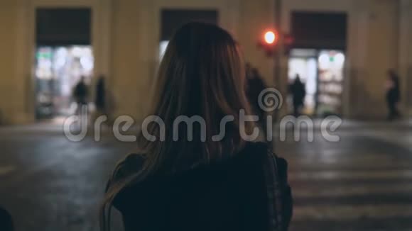 年轻的黑发女人在晚上穿过交通道路独自走在市中心穿过街道视频的预览图