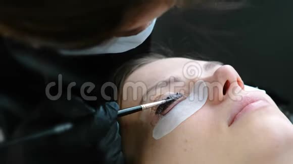美容治疗美容师在睫毛上涂上黑色油漆复合睫毛特写面部侧视视频的预览图