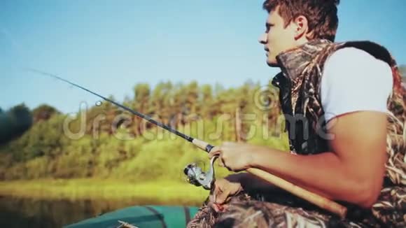 独自一人坐在橡皮船上在湖边钓鱼公鱼握着鱼竿抓住咬人的鱼视频的预览图