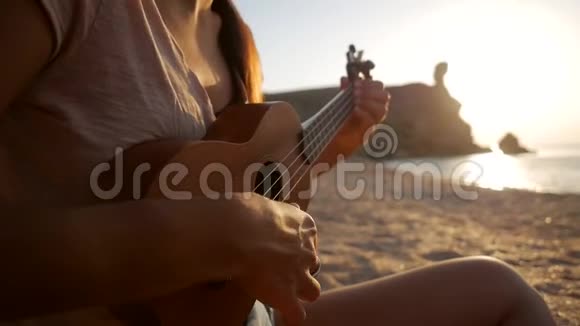 女孩坐在沙滩上弹着四弦琴吉他关闭高清慢镜头视频的预览图