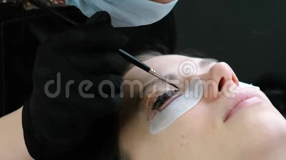 美容治疗美容师在睫毛上涂上黑色油漆复合睫毛特写面部侧视视频的预览图