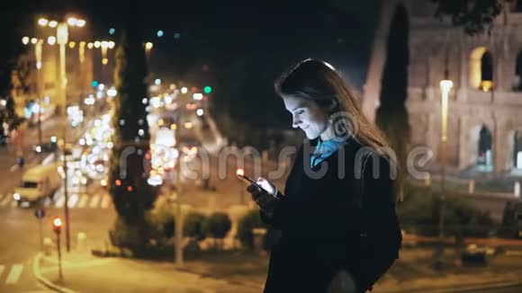 美丽的女人站在意大利罗马的交通道路和竞技场附近使用智能手机的肖像视频的预览图