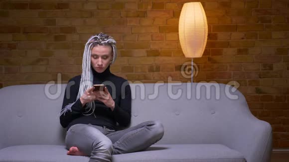 一位年轻迷人的白种人潮女用手机在舒适的室内沙发上拍摄特写镜头视频的预览图