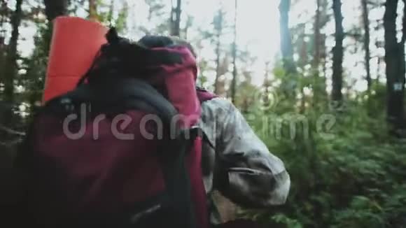 清晨独自穿着迷彩制服的年轻人背着背包和旅游垫穿过森林视频的预览图