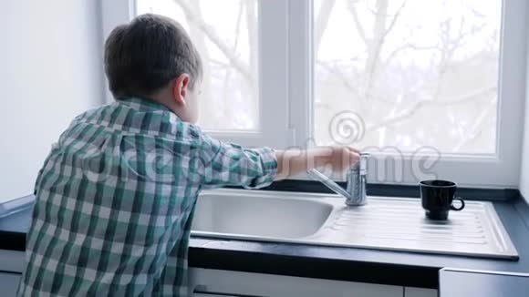 家里的日常生活小男孩在窗户的背景下在水槽里洗餐具视频的预览图