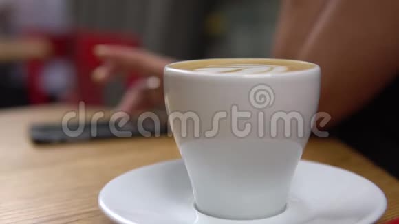 年轻女子喝着咖啡坐在室内的城市咖啡馆里使用智能手机视频的预览图